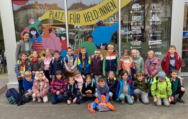 Eine Gruppe von Kindern in Winterkleidung posiert für ein Foto vor einem Gebäude mit farbenfrohen Zeichentrickfiguren auf den Glasfenstern.