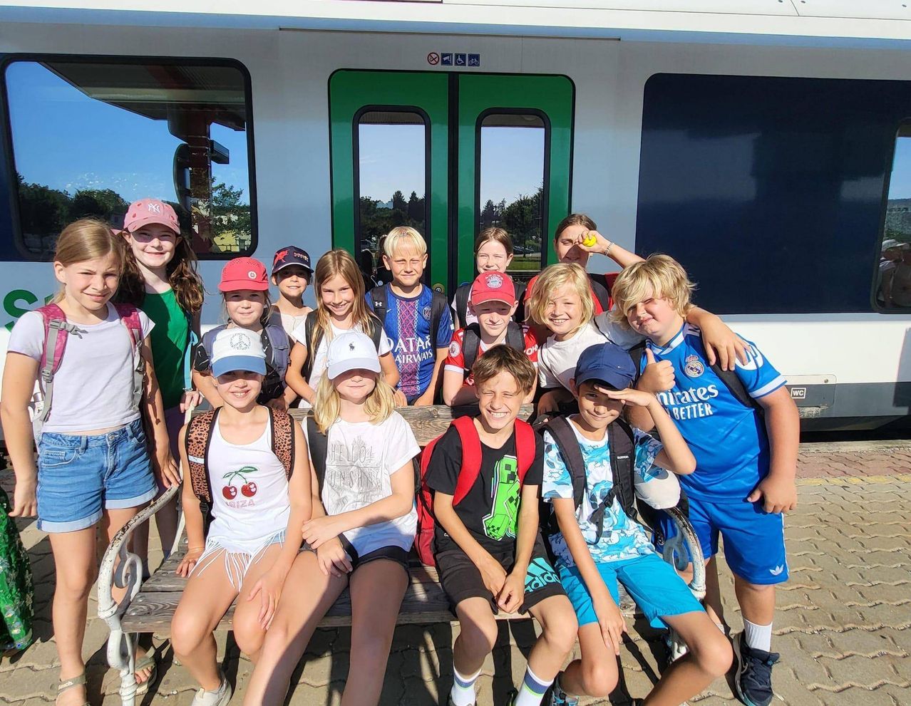 Eine Gruppe von Kindern und Jugendlichen posiert für ein Foto vor einem Zug, einige tragen Hüte und Rucksäcke.