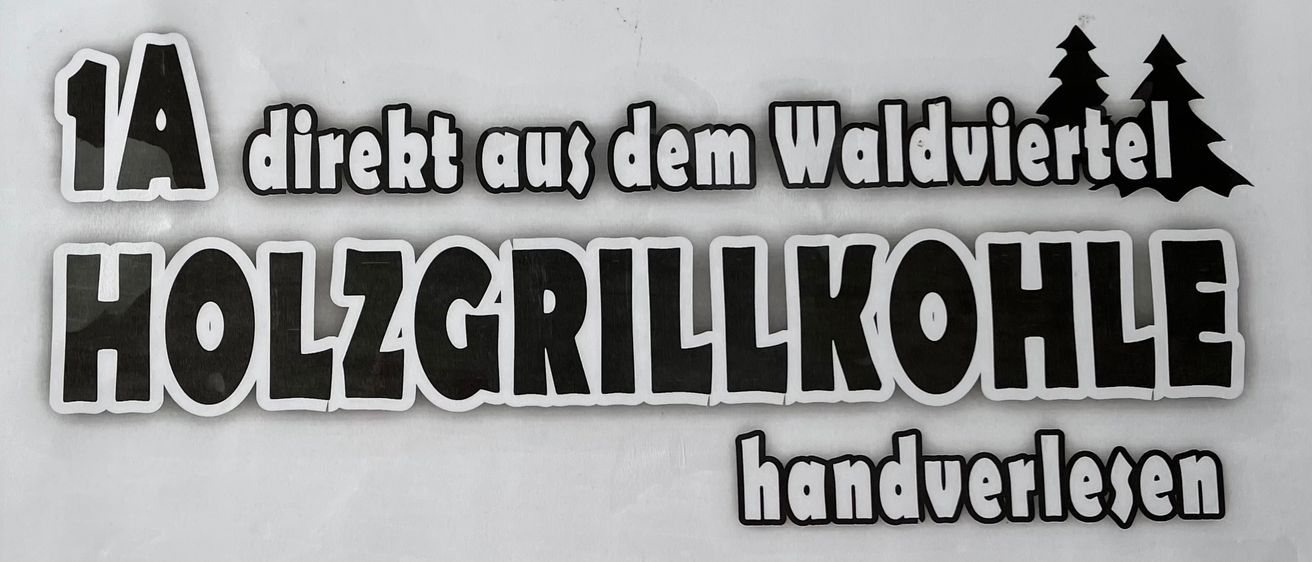 Ein weißer Poster mit schwarzem Text steht 'direkt aus dem Waldvieh.' Darunter steht 'HOLZGRILLKOFFEE' in großen schwarzen Buchstaben. Darunter steht 'die Besondere' für den Preis.