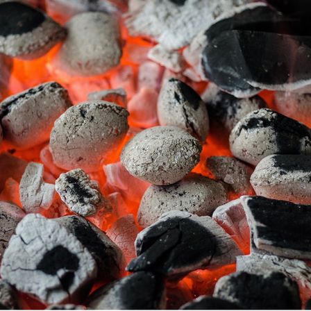 Ein Nahaufnahme von brennender Kohle mit glühenden Glut und einer Mischung aus schwarzen und grauen Kohlen.