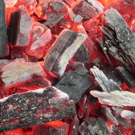 Nahaufnahme von brennender Holzkohle mit verschiedenen Größen und Formen, die orange und rote Flammen abgeben.