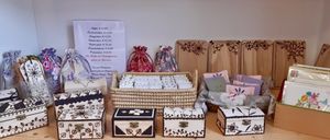 Eine Ausstellung dekorativer Holzkisten und Tüten, mit einem Schild, das Preise und Artikel auflistet. Körbe gefüllt mit kleinen Gegenständen und blumengeschmückte Holzbretter sind ebenfalls vorhanden.