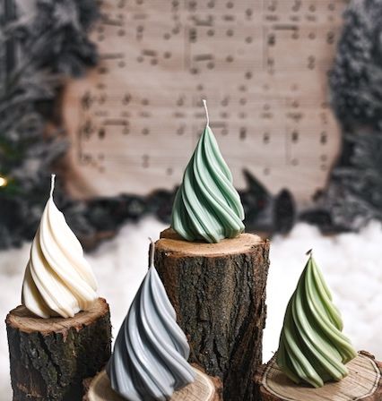 Vier weihnachtsbaumförmige Kerzen stehen auf Baumstümpfen. Dahinter ist ein verschwommener Hintergrund mit Musiknoten und Bäumen.