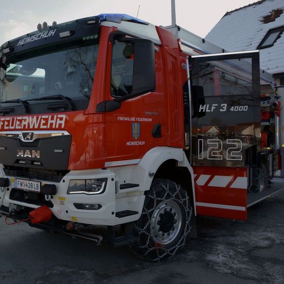Ein roter Feuerwehrwagen aus Heimschuh mit der Nummer 122 steht mit Schneeketten an seinen Reifen auf der Straße geparkt.