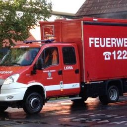 Ein roter und weißer Feuerwehrwagen mit den Worten 'Feuerwehr' und '122' steht vor einem Gebäude.