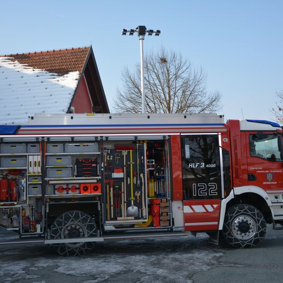 Ein roter Feuerwehrwagen ist draußen geparkt, seine Türen offen und zeigen eine Reihe von Werkzeugen und Ausrüstung. Der Wagen ist mit der Nummer 122 gekennzeichnet und scheint einsatzbereit zu sein.