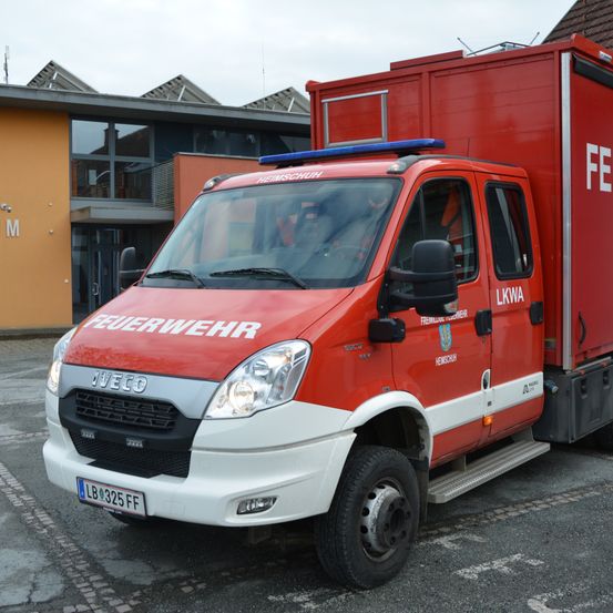 Ein roter und weißer Iveco-LKW, gekennzeichnet mit 'Feuerwehr', steht vor einem Gebäude mit Solarpanelen. Der LKW hat ein blaues Licht oben und ein Kennzeichen LB 325 FF.