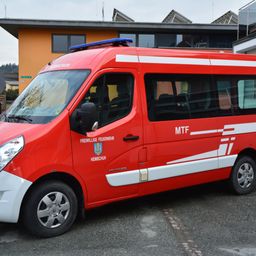 Ein rotes Fahrzeug, beschriftet mit 'MTF' und 'FREIWILLIGE FEUERWEHR HEIMSCHUH,' geparkt vor einem gelben Gebäude mit Solarmodulen.