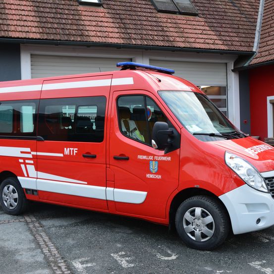 Ein rotes Notfallfahrzeug mit weißen Markierungen ist vor einem roten Gebäude mit Ziegeldach und Fenstern geparkt. Das Fahrzeug hat die Buchstaben MTF an der Seite.