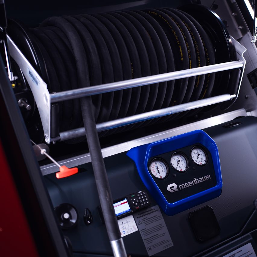 Nahaufnahme eines schwarzen Industriegeräts mit einer Schlauchtrommel, Manometern und einem blauen Kunststoffteil mit der Aufschrift 'Rosenbauer'.