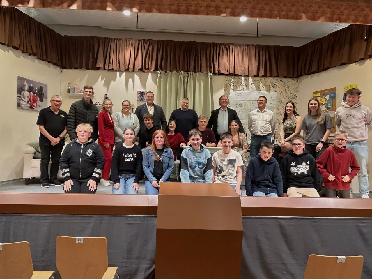 Eine Gruppe von Erwachsenen und Kindern posiert für ein Foto im Theater, einige stehen und andere sitzen.
