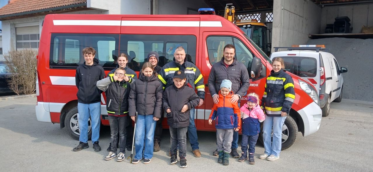 Eine Gruppe von Kindern und Erwachsenen, einschließlich Feuerwehrleuten, posiert vor einem roten Feuerwehrauto. Sie sind alle warm gekleidet.