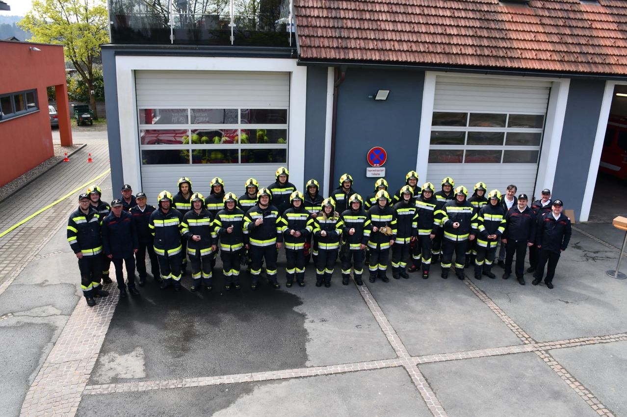 Eine Gruppe von Feuerwehrleuten in gelben und schwarzen Uniformen posiert für ein Foto vor einer Feuerwache.
