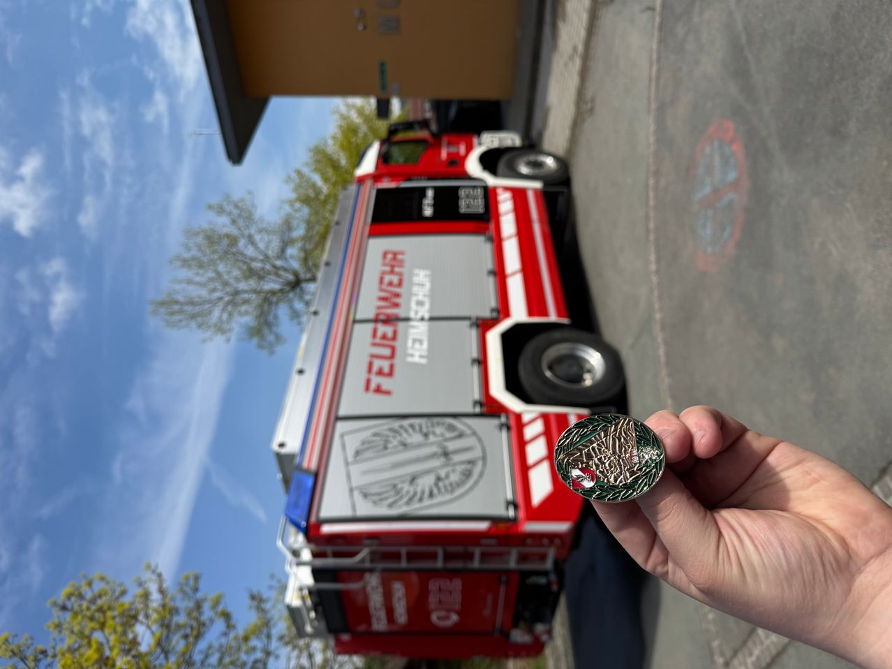 Ein Feuerwehrfahrzeug ist am Straßenrand geparkt, und eine Person hält eine Münze mit einem Feuerwehremblem.