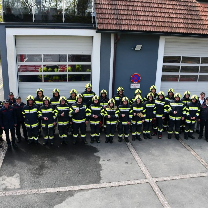 Eine Gruppe Feuerwehrleute in Uniform posiert für ein Foto vor einer Feuerwache.