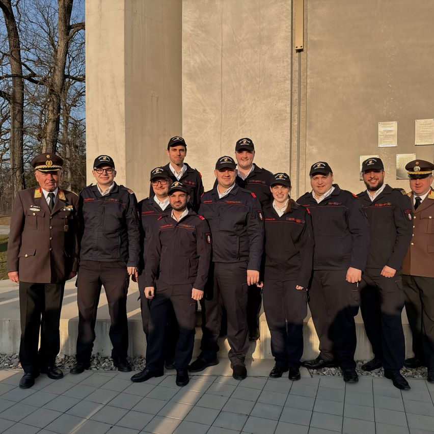 Eine Gruppe uniformierter Personen steht vor einer Betonstruktur mit Plaketten, wahrscheinlich für ein offizielles Foto.