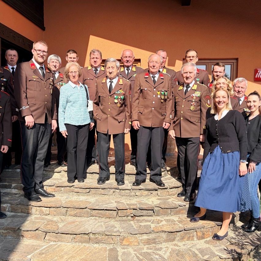 Eine Gruppe von Männern und Frauen in Militäruniformen steht auf Steinstufen vor einem Gebäude, mit einigen Personen dahinter. Sie alle scheinen zu lächeln und posieren für ein Foto.