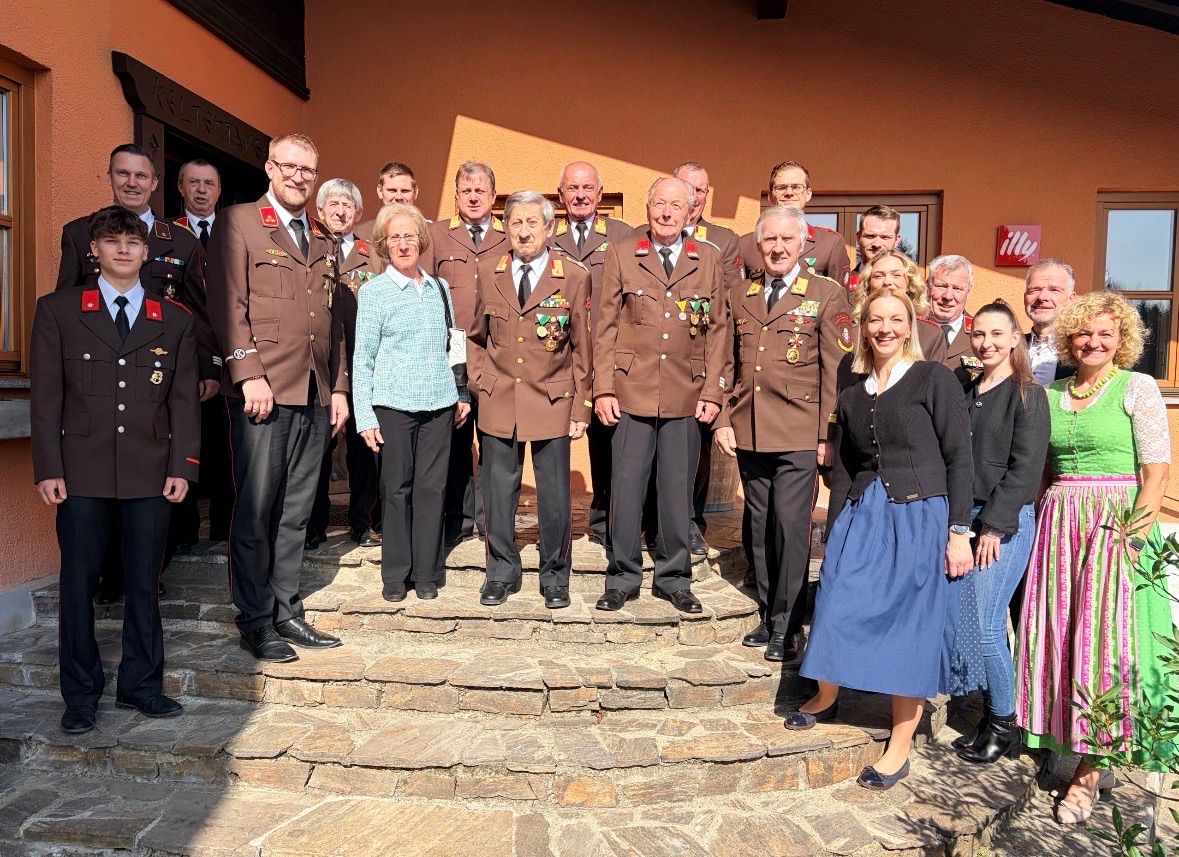 Eine Gruppe von Männern und Frauen in Militäruniformen steht auf Steinstufen vor einem Gebäude, mit einigen Personen dahinter. Sie alle scheinen zu lächeln und posieren für ein Foto.