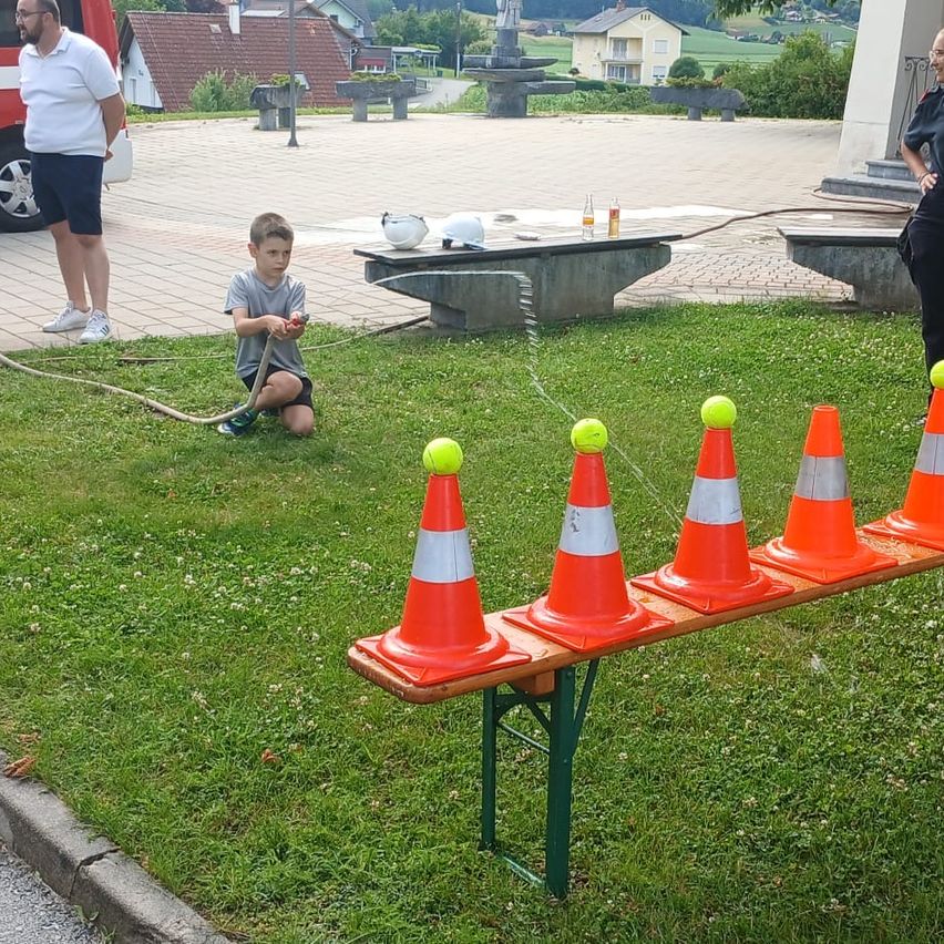 Ein junger Junge schlägt Tennisbälle von orangefarbenen Kegels in einem Park. Ein Mann steht in der Nähe und eine Frau beobachtet.