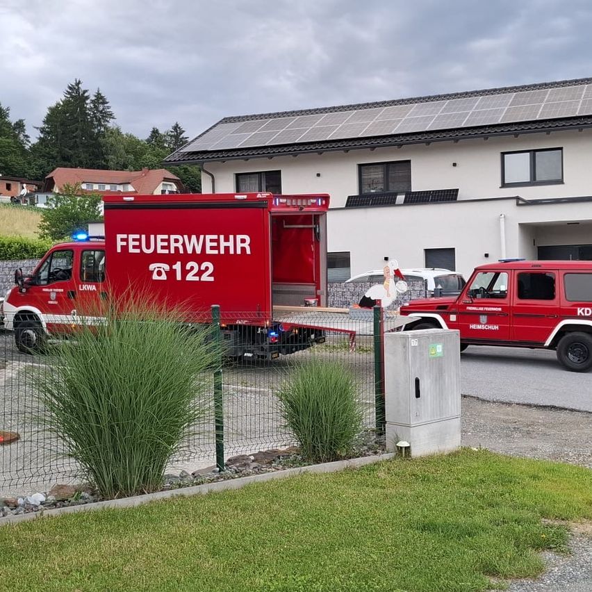 Ein roter Feuerwehrwagen mit der Aufschrift 'FEUERWEHR 122' steht vor einem Gebäude mit Solarpanelen. Ein weiteres rotes Fahrzeug ist dahinter geparkt.
