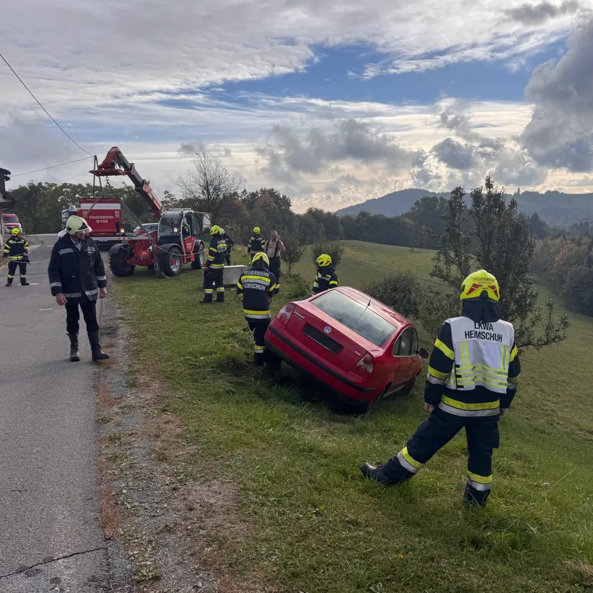 Ein rotes Auto ist am Straßenrand beschädigt. Rettungskräfte sind vor Ort, einschließlich einer Person mit gelbem Helm.