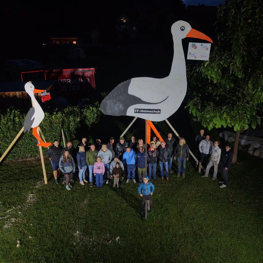 Eine Gruppe von Menschen posiert für ein Foto vor einer großen Storchstatue bei Nacht.