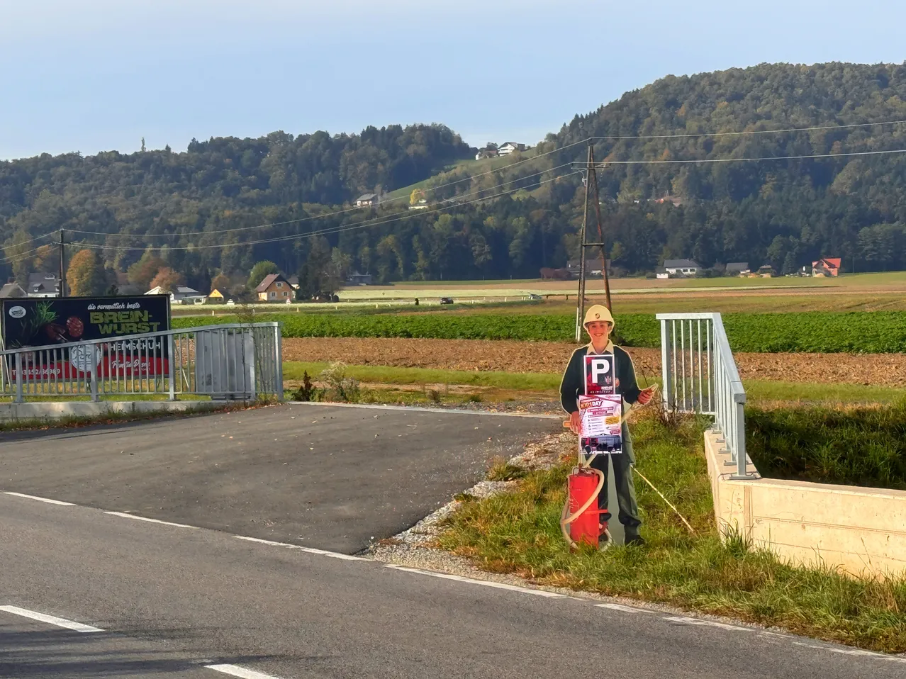 Eine Person steht am Straßenrand mit einem Schild, das 'P' und einen roten Feuerlöscher zeigt.