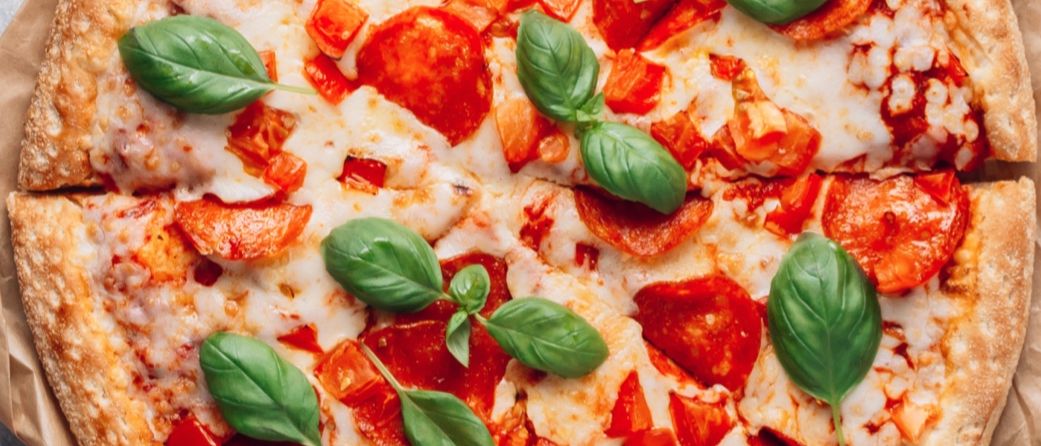 Eine Nahaufnahme einer Pizza mit geschmolzenem Käse, roten Pepperoni und frischen Basilikumblättern.