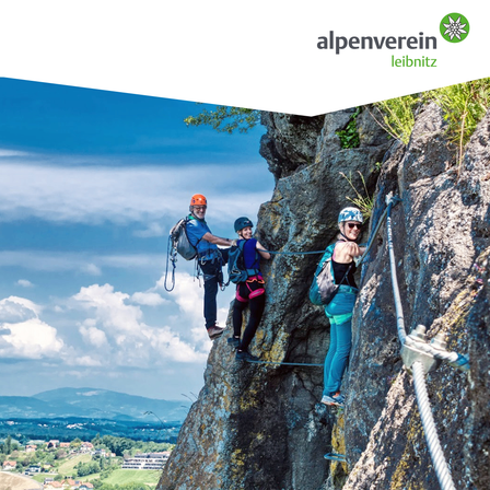 Drei Personen klettern am Fels und tragen Sicherheitsausrüstung. Eine steht vorne, zwei dahinter, verbunden durch Seile. Im Hintergrund sieht man ein Tal mit Bergen und Häusern.