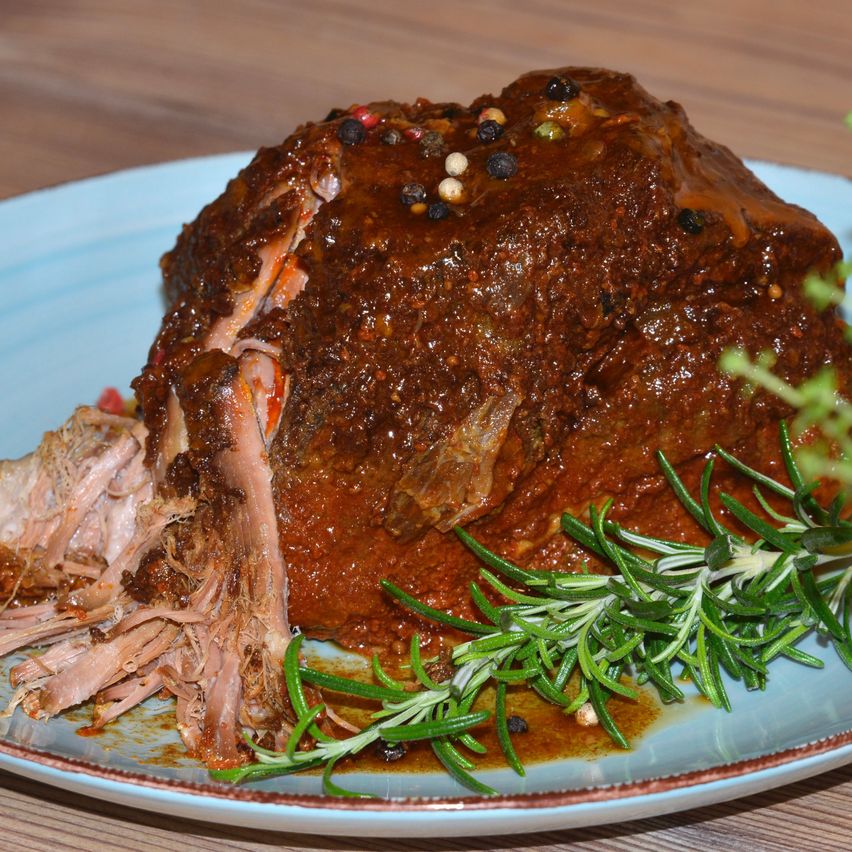 Ein Teller mit langsam gekochtem Rinderbraten, bedeckt mit einer reichen, dunklen Sauce, mit Rosmarin garniert auf einem Holztisch.
