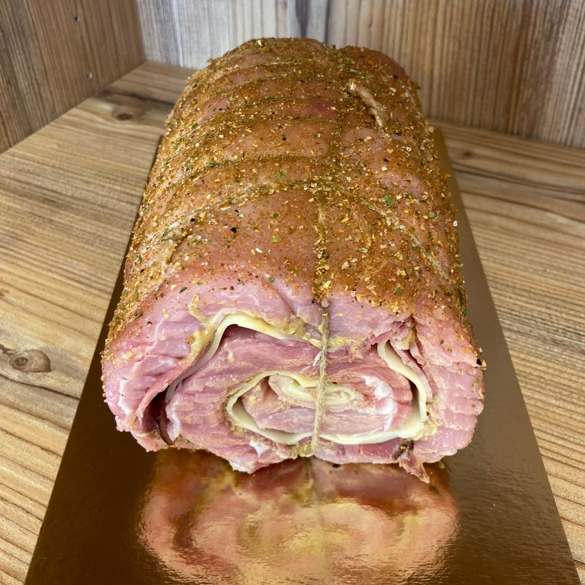 Ein fest gerollter Schinken, mit Kräutern gewürzt, liegt auf einem Holztisch. Er ist in Schnur eingewickelt und hat eine goldbraune Kruste.