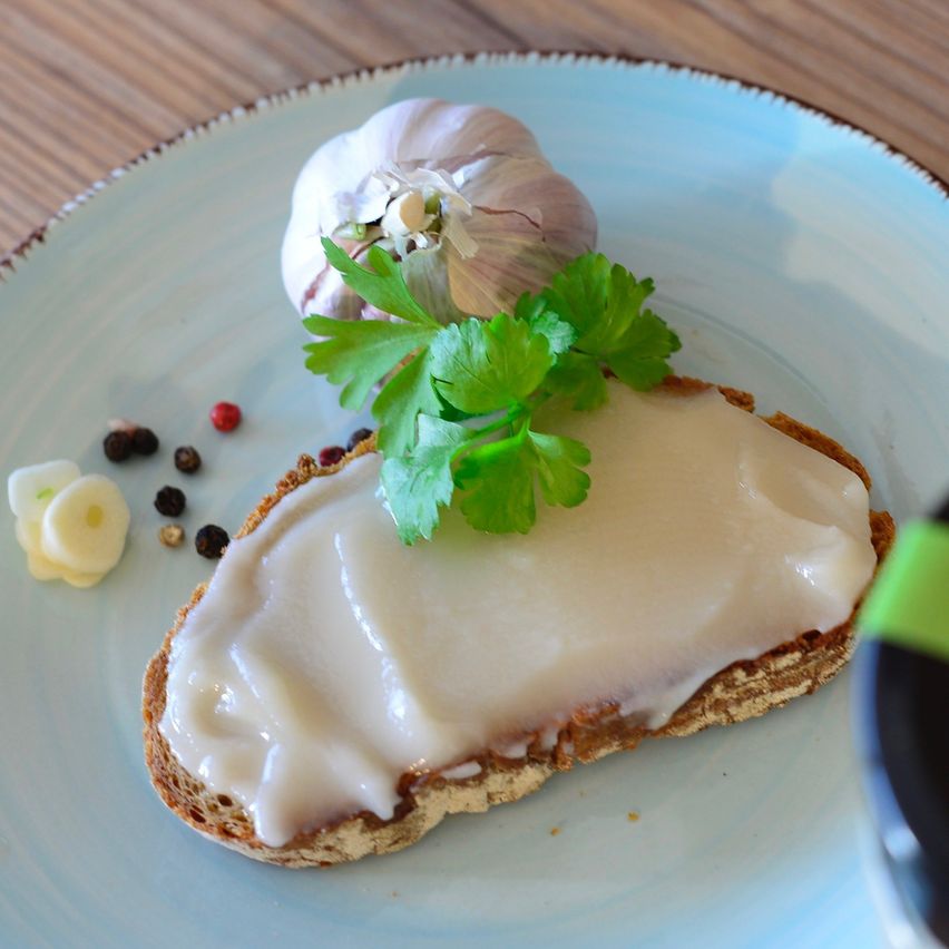 Ein Stück Brot mit weißer Creme, garniert mit Petersilie, steht auf einem blauen Teller mit Knoblauch und Pfeffer.