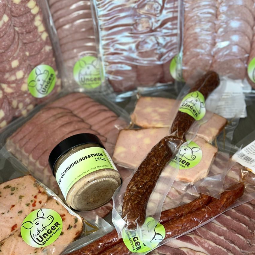 Eine Auswahl an verpackten Fleischsorten, einschließlich Würste, Salami und geschnittenem Fleisch, alle mit grünen Etiketten, die 'Ungen' und 'Biohof Ungen' lesen. Im Vordergrund befindet sich ein Glas 'Gammelaufstrich' und eine Wurst in Plastik.