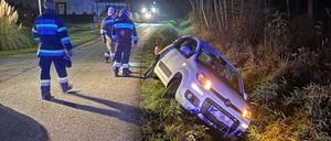 Ein Auto liegt nachts auf dem Landweg auf der Seite, drei Feuerwehrleute sind vor Ort. Das Fahrzeug steht an einem Grasstreifen.