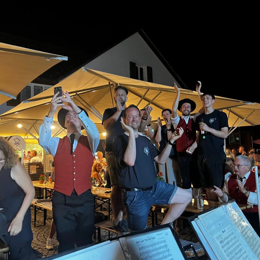 Eine Gruppe von Menschen feiert bei Nacht unter einem Zelt, einer Mann macht ein Foto mit seinem Handy.