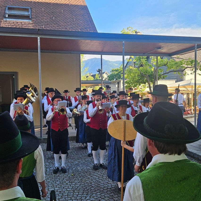 Eine Gruppe von Musikern in traditioneller Kleidung spielt im Freien, mit Bergen im Hintergrund.