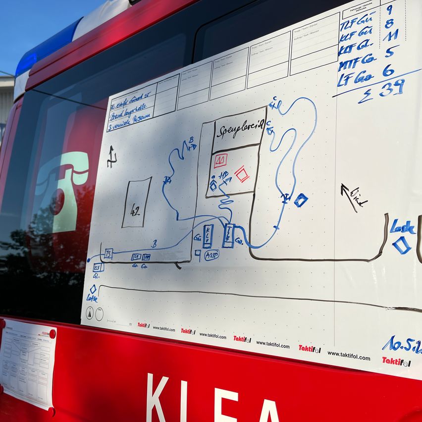 Eine Tafel an der Seite eines roten Fahrzeugs zeigt eine Karte mit verschiedenen Routen, gekennzeichnet durch Zahlen und Pfeile. Beschriftungen sind 'Spreylored' und 'Look.' Der Hintergrund ist ein blauer Himmel.