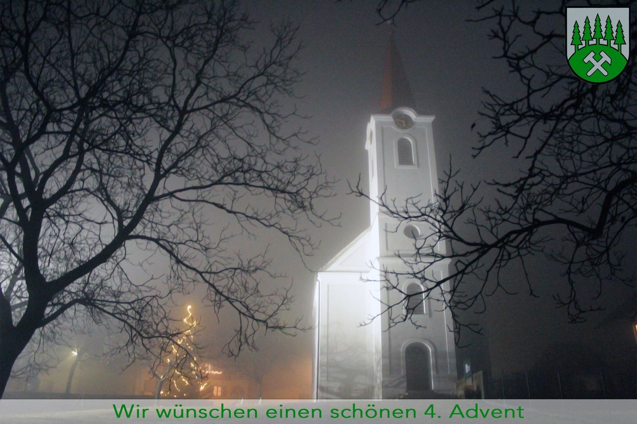 Ein weißer Kirchturm mit einem Spitzturm ist im Nebel zu sehen. Ein beleuchteter Weihnachtsbaum steht vor der Kirche.