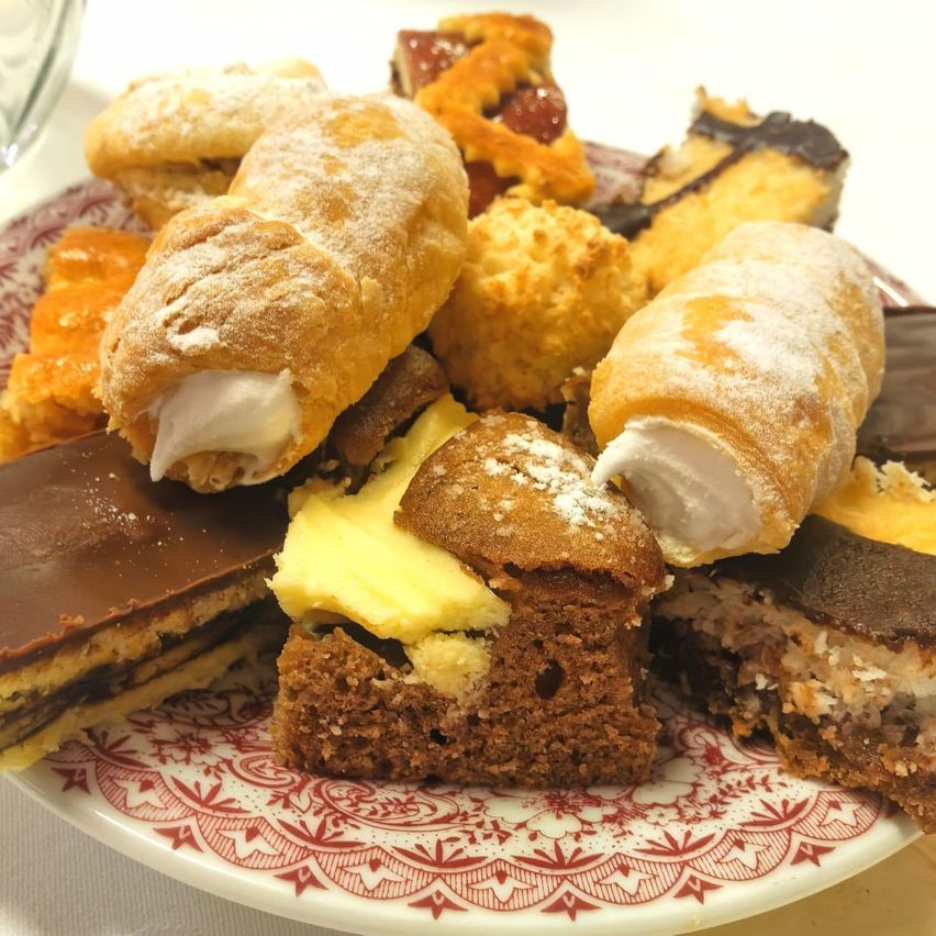 Ein Teller mit verschiedenen Gebäckstücken, darunter Croissants, Cremepuffs und Schokoladenüberzogene Desserts mit weißer und brauner Glasur.