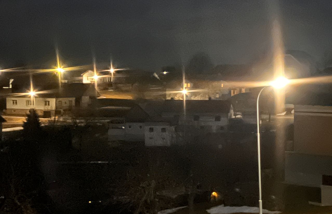 Ein nächtlicher Blick auf eine kleine Stadt mit mehreren Häusern und Straßenlaternen, die das Gebiet erhellen und inmitten der Dunkelheit ein warmes Leuchten erzeugen.