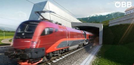 Ein roter Zug fährt durch einen Tunnel auf einer Bahnstrecke, mit einem Grasfeld auf der rechten Seite und Bergen in der Ferne.