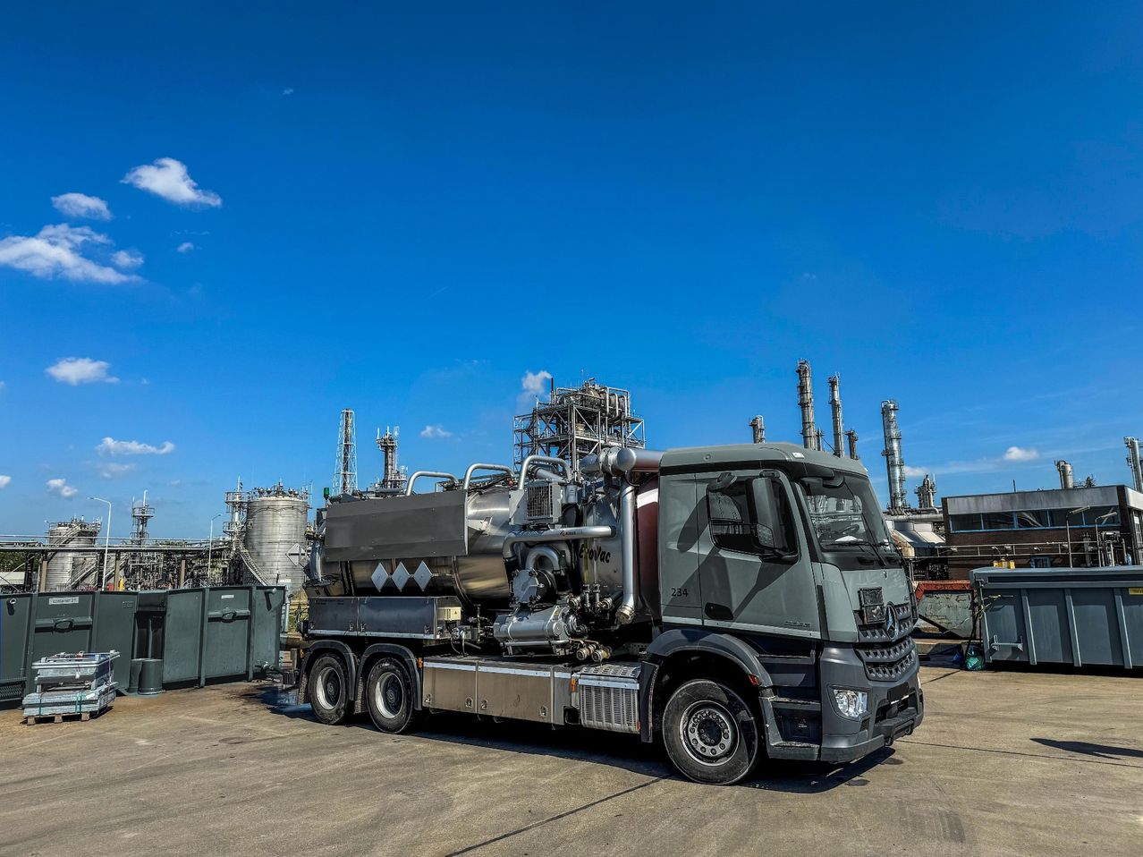 Ein großer Industrielastwagen ist vor einer Fabrik mit blauem Himmel und Wolken geparkt. Der Lastwagen hat einen großen Tank am Heck.