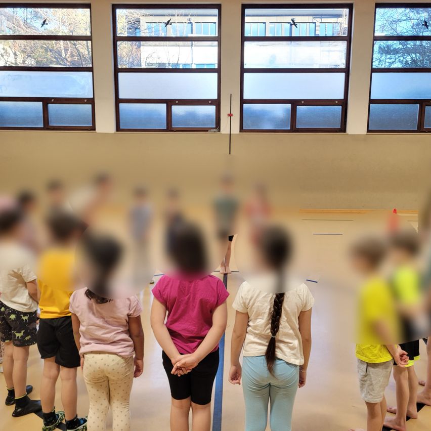 A blurry image of a group of children in a gymnasium with large windows and a person standing in the middle.