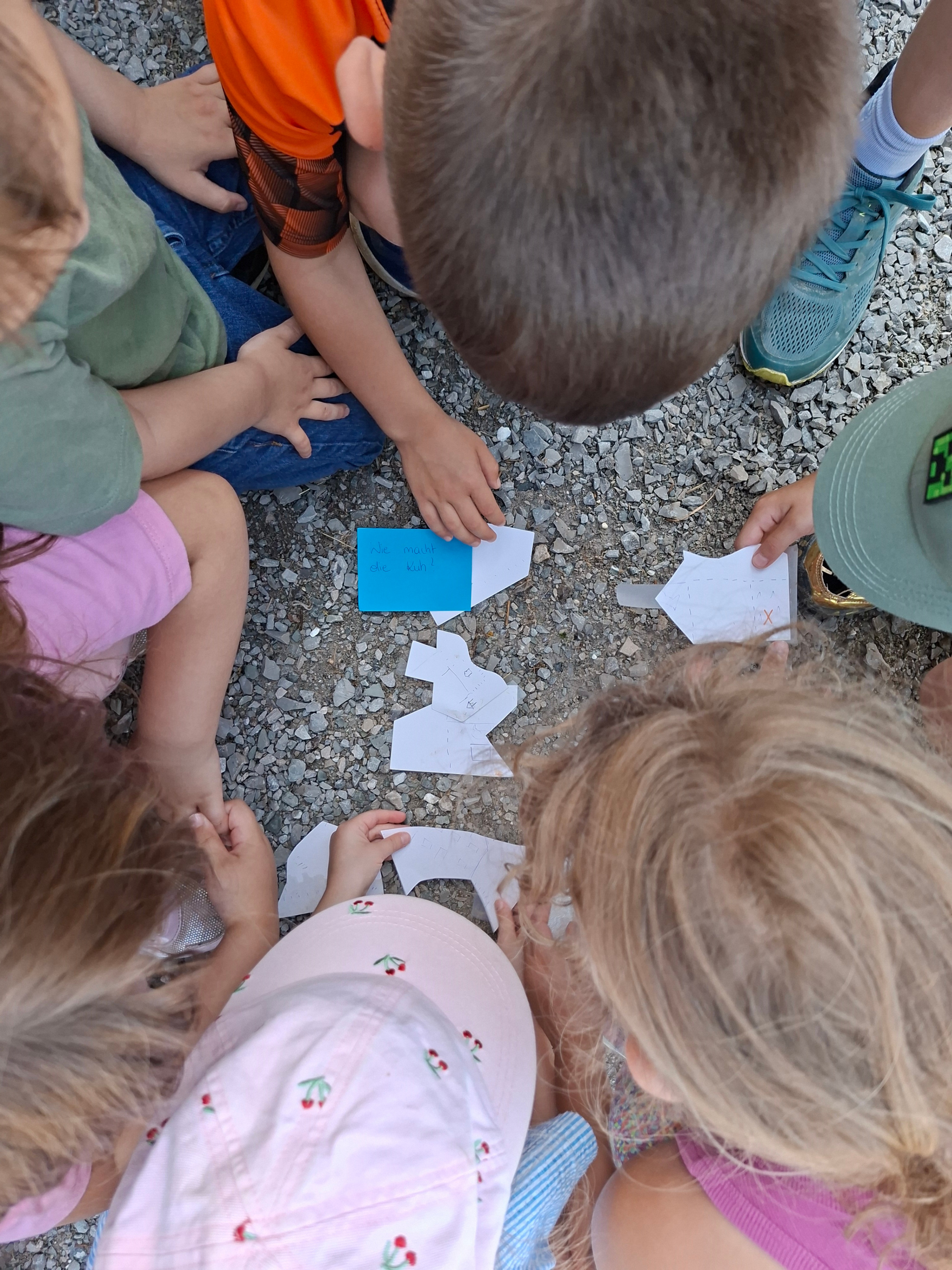 Kinder basteln mit Papier und schreiben auf einem Zettel „Wie macht die Kuh?“.