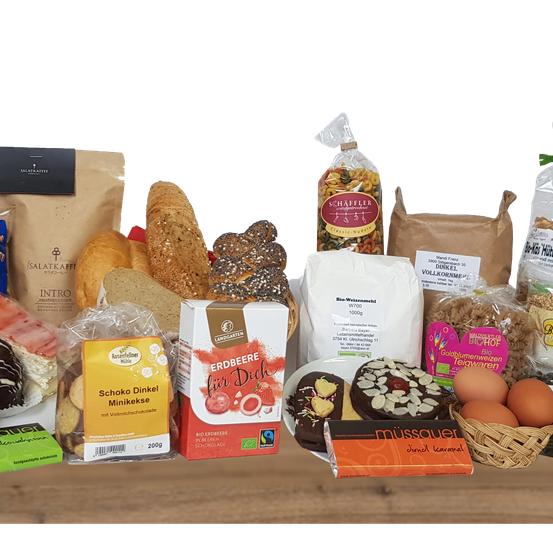 Eine Vielzahl von Lebensmitteln ist auf einem Tisch ausgestellt. Es gibt Tüten mit Nudeln, Keksen und anderen Produkten. Einige Artikel haben Etiketten auf Deutsch.