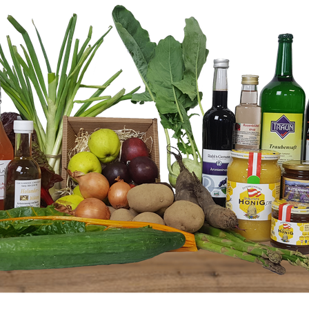 Eine Sammlung von Gemüse, Früchten und Gewürzen ist auf einer Holzoberfläche ausgestellt. Das Sortiment umfasst grüne Blattgemüse, Zwiebeln, Kartoffeln und eine Gurke.