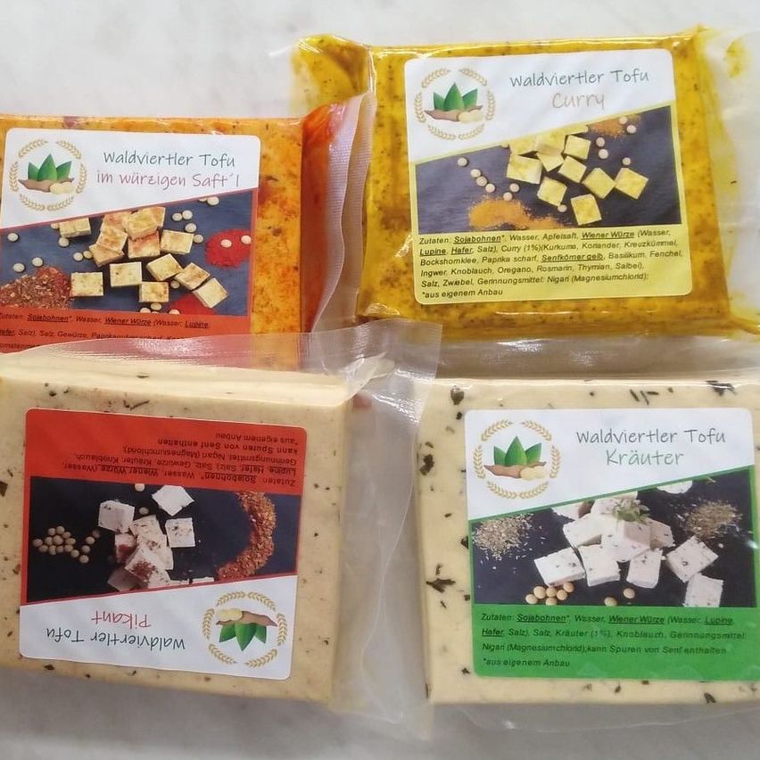 Vier Packungen Tofu in verschiedenen Geschmacksrichtungen sind abgebildet, darunter Curry, Kräuter und scharf. Jede Packung ist mit ihrem Geschmack und den Zutaten beschriftet.