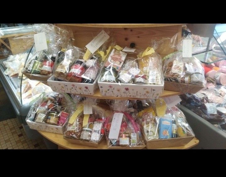 Ein Regal zeigt verschiedene Geschenkboxen mit unterschiedlichen Lebensmitteln und Gewürzen, alles ordentlich in Plastik verpackt. Die Boxen sind auf einem Holzregal in einem Geschäft angeordnet.