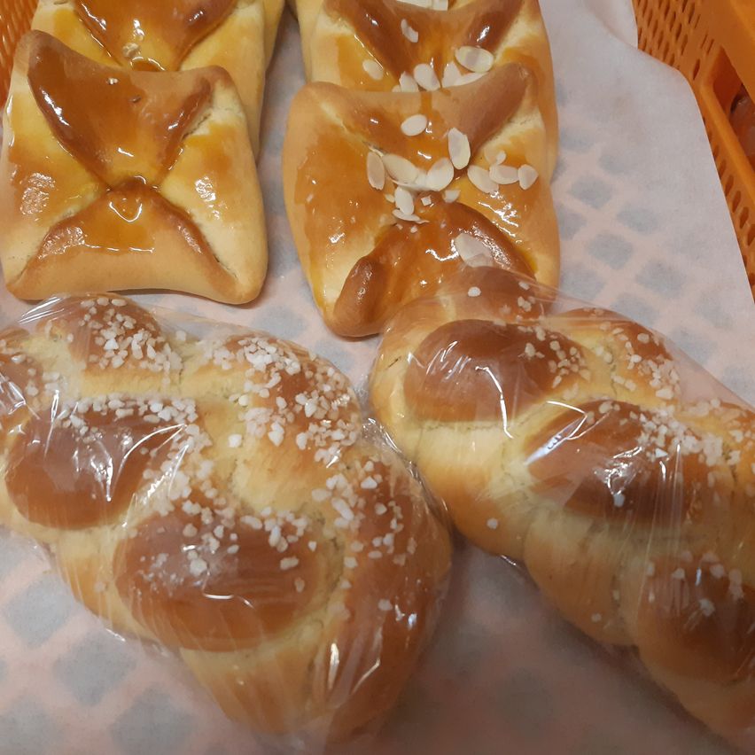 Vier mit Mandeln und Sprenkeln verzierte Brote mit Glasur, in Plastik verpackt und auf einer strukturierten Oberfläche platziert.