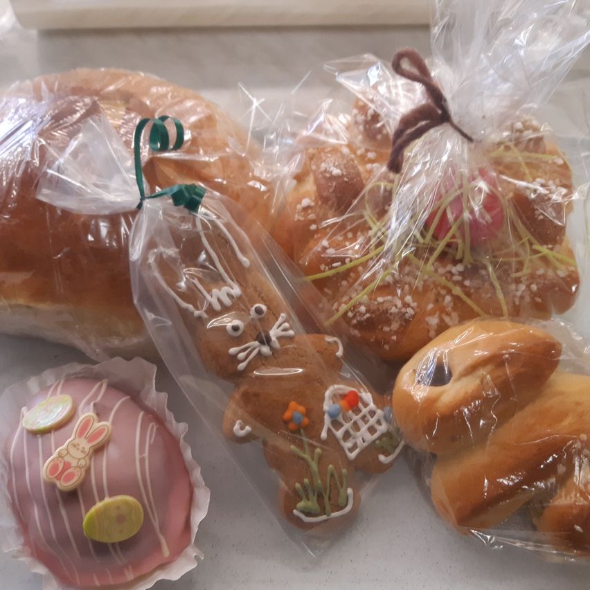 Mehrere Ostergebäcke in Plastiktüten, darunter ein rosa Ostereierkuchen, ein Schokoladenhase und ein Laib Brot. Alle Artikel sind für Ostern dekoriert.
